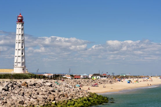 Lighthouse by beach with people and ocean view.